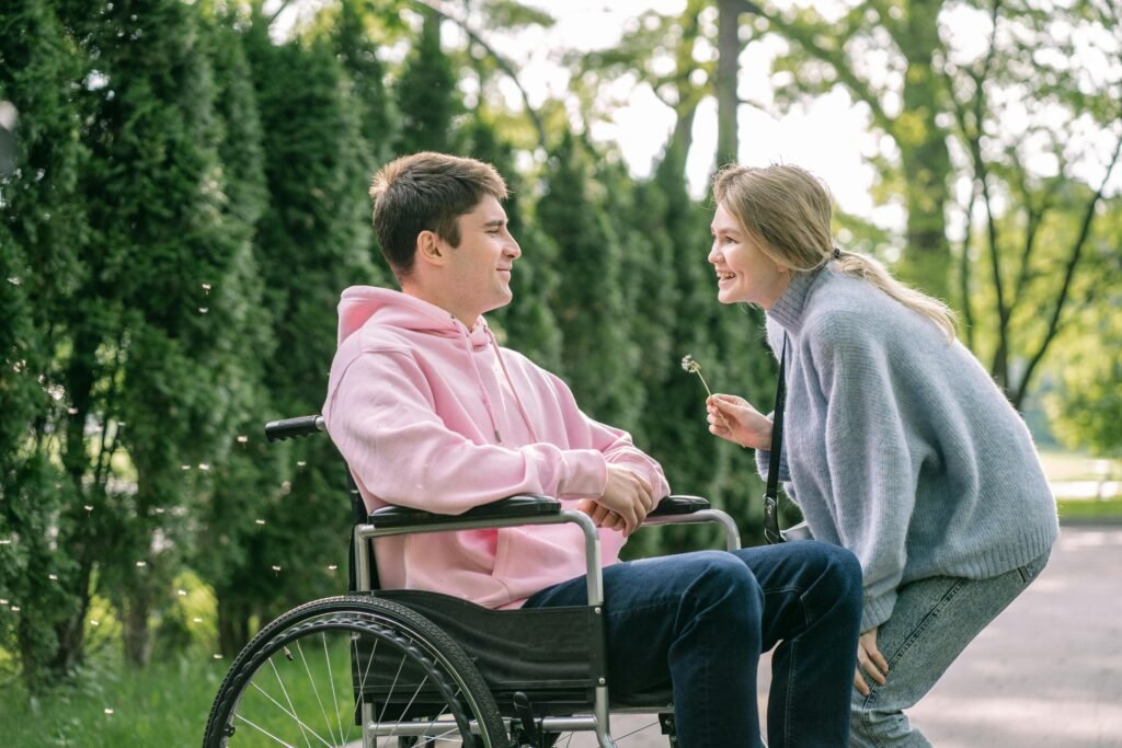 pexels-photo-8415707-8415707 A young man in a wheelchair enjoys a cheerful moment with a woman outdoors.